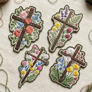 May include: Four embroidered patches featuring brown wooden crosses adorned with various colorful flowers and green leaves. Each patch displays a unique arrangement of blossoms, including pink, yellow, blue, and white petals, stitched onto a light fabric base.