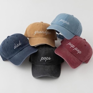 May include: A collection of six baseball caps in various colors, including navy, tan, black, and burgundy. Each cap features white embroidered text: "dad", "grandpa", "pops", "papa", and "pap pap".