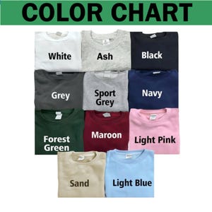May include: A color chart displaying eleven crewneck sweatshirts in various colors labeled White, Ash, Black, Grey, Sport Grey, Navy, Forest Green, Maroon, Light Pink, Sand, and Light Blue. Each sweatshirt features a visible brand tag at the neck.