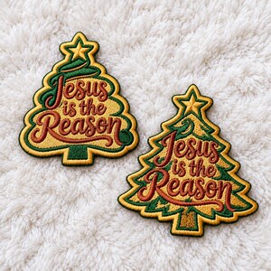 May include: Two embroidered patches shaped like Christmas trees with yellow centers and green borders. Each patch features a gold star at the top and the brown embroidered text "Jesus is the Reason" written in a cursive script across the center.