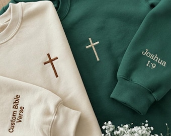 May include: A cream sweatshirt with a brown embroidered cross and the text Custom Bible Verse on the sleeve, alongside a dark green sweatshirt with a white embroidered cross and the text Joshua 1:9 on the sleeve, both featuring crew necklines.