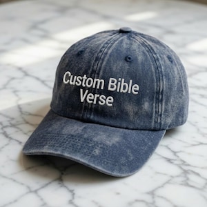 May include: A denim blue baseball cap with the text "Custom Bible Verse" embroidered in white. The cap has a curved brim and a button on top. The fabric has a faded, vintage look.