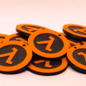 Puede incluir: Una colección de fichas circulares naranjas y negras. Cada ficha presenta un centro negro con un símbolo y borde naranja. Las fichas están dispersas, algunas superpuestas, sobre un fondo claro.