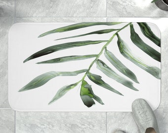 Puede incluir: Alfombra de baño blanca con un diseño de hoja verde en acuarela. La hoja está estilizada y tiene una forma fluida y orgánica.