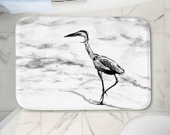 May include: A black and white bathroom rug with a watercolour-style illustration of a heron standing on a beach.