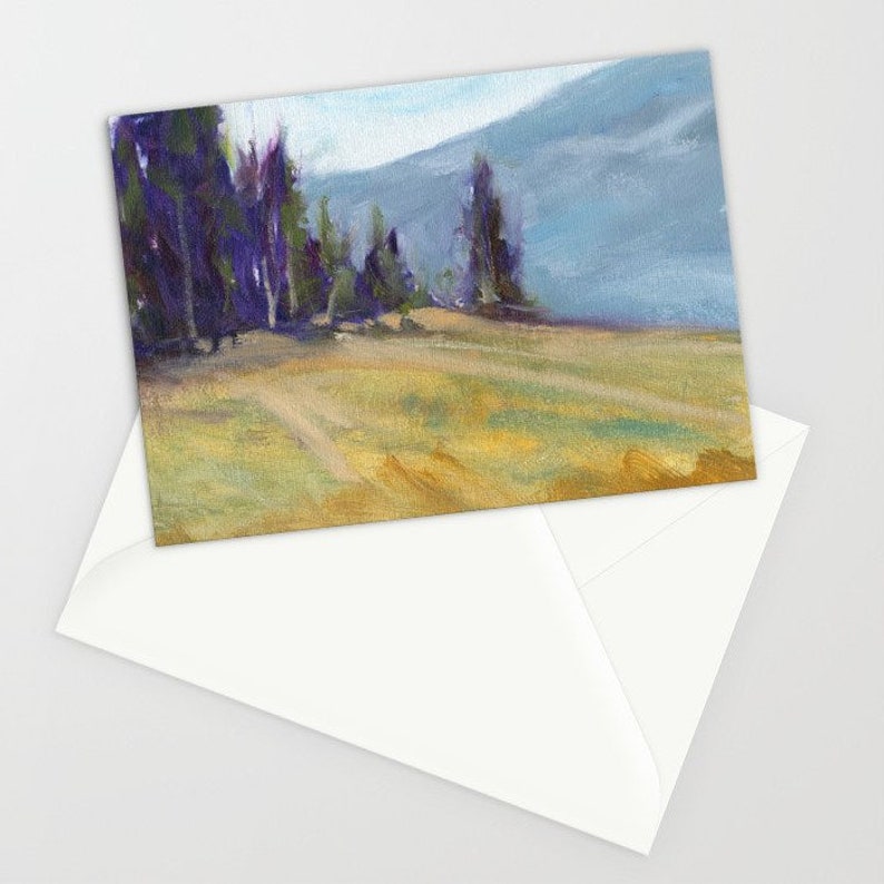 May include: A landscape art print depicting a field of yellow and green grass, tall purple trees, and a blue mountain range. The artwork is presented on a white card, partially visible within a white envelope.