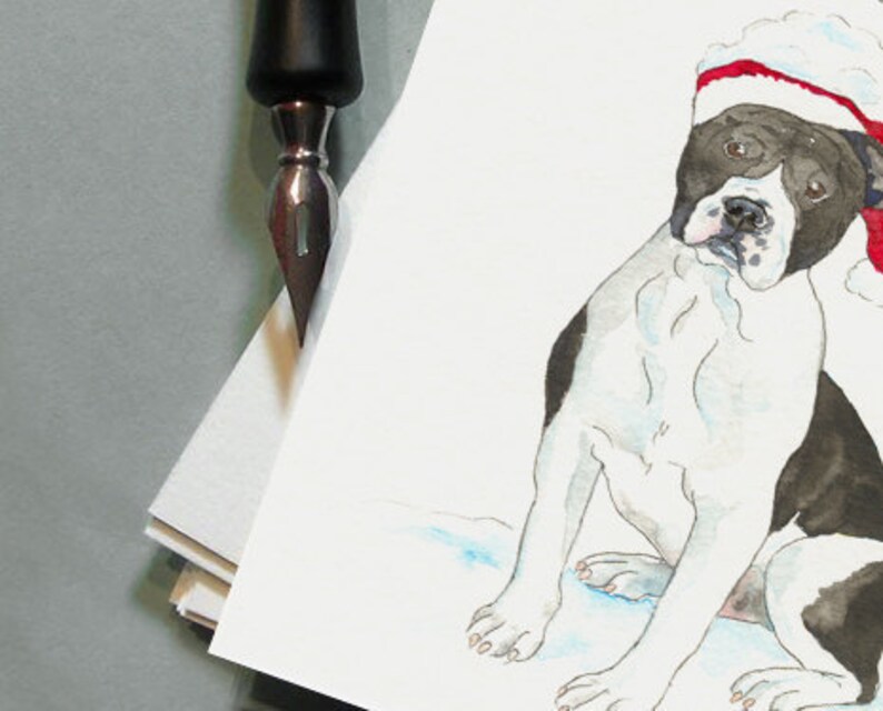 K&ouml;nnte beinhalten: Aquarellmalerei eines schwarz-wei&szlig;en Hundes mit Weihnachtsm&uuml;tze. Der Hund sitzt mit leicht geneigtem Kopf. Eine schwarze Feder ist in der oberen linken Ecke, mit einem Stapel wei&szlig;em Papier.