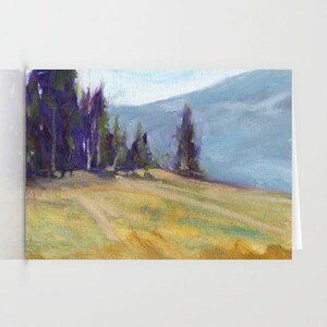 May include: A landscape painting on a greeting card. The artwork shows a field of yellow and green grass, with a line of trees in the background. A mountain range is visible in the distance, under a light blue sky.