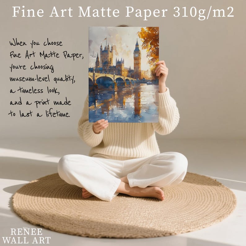 A person is sitting on a round rug, holding up a framed painting of a cityscape with a castle in the background.