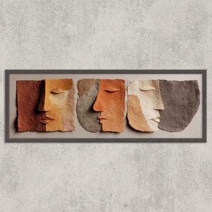 Puede incluir: Una obra de arte enmarcada que presenta tres rostros abstractos con los ojos cerrados. Los rostros están compuestos de papel texturizado en tonos tierra de marrón, naranja y crema. La obra está sobre un fondo gris neutro.