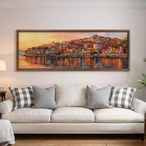 May include: A framed watercolour painting shows a vibrant cityscape at sunset, reflected in the water. The artwork hangs above a white sofa with grey and chequered cushions.