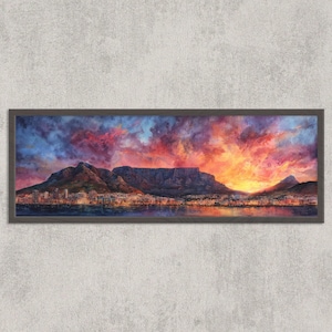 Puede incluir: Pintura de paisaje enmarcada que representa una vibrante puesta de sol sobre una ciudad y montañas. El cielo es una mezcla de tonos rojos, naranjas y azules. La obra de arte está enmarcada en un marco gris oscuro, montada en una pared gris texturizada.