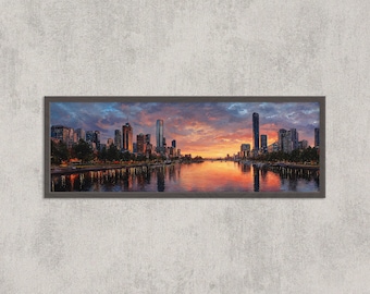 May include: Panoramic framed print of a cityscape at sunset. The artwork depicts a river reflecting the colorful sky and the silhouettes of buildings. The frame is dark gray, and the overall scene is vibrant with orange, blue, and purple hues.
