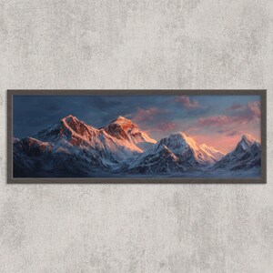 May include: A framed print depicting a mountain range at sunset. The snow-covered peaks are bathed in golden light, set against a dark blue sky and pink clouds. The frame is a dark grey colour.