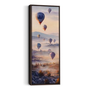 以下が含まれることがあります： 水彩画の熱気球が霧のかかった風景の上を飛んでいる、縦長の額装アートプリント。気球は青、紫、オレンジなど様々な色があります。このアートワークは、静けさと冒険の感覚を呼び起こします。