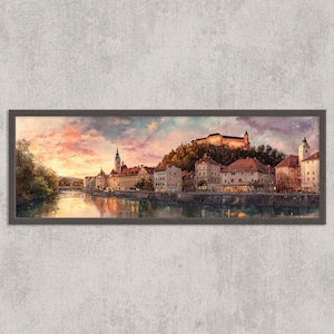 May include: A framed panoramic painting of a European city at sunset. The artwork depicts buildings along a river, with a castle on a hill. The sky is filled with pink, orange, and purple hues, reflecting in the water.