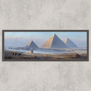 May include: A framed print showing the pyramids of Giza in Egypt. The artwork depicts three pyramids, the Sphinx, and camels in a desert landscape. The colour palette includes shades of tan, blue, and brown.