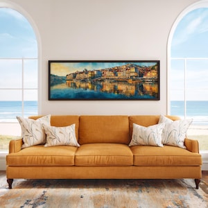 May include: A mustard-colored sofa with three cushions and four decorative pillows. Above the sofa is a framed panoramic watercolor painting of a cityscape reflected in water. The room has large arched windows overlooking the ocean.