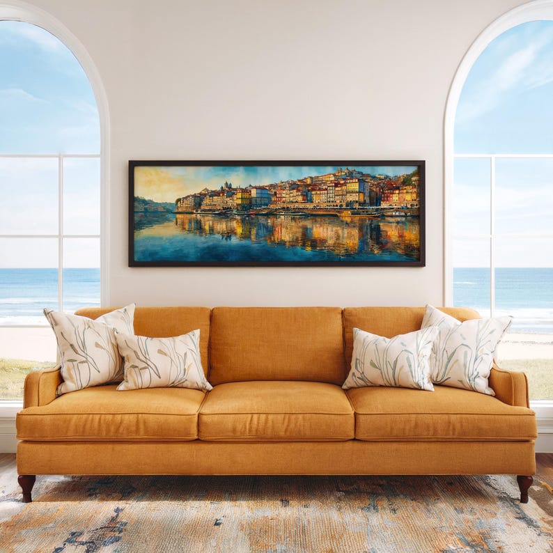 May include: A mustard-colored sofa with three cushions and four decorative pillows. Above the sofa is a framed panoramic watercolor painting of a cityscape reflected in water. The room has large arched windows overlooking the ocean.