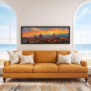 Pu&ograve; includere: Un dipinto panoramico incorniciato di Firenze, Italia, con un vivace cielo al tramonto. L'opera d'arte &egrave; appesa sopra un divano color senape con cuscini decorativi. La stanza ha grandi finestre ad arco con vista sull'oceano.
