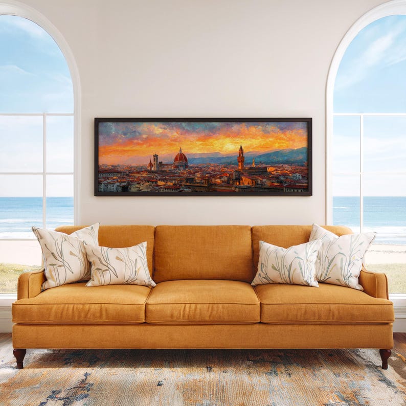 Pu&ograve; includere: Un dipinto panoramico incorniciato di Firenze, Italia, con un vivace cielo al tramonto. L'opera d'arte &egrave; appesa sopra un divano color senape con cuscini decorativi. La stanza ha grandi finestre ad arco con vista sull'oceano.