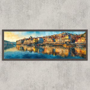 May include: A framed watercolor painting of a cityscape with colorful buildings along a river. The artwork features a vibrant sky with yellow and blue hues, reflecting in the water below. The frame is dark brown.