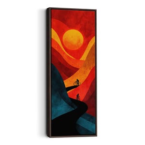 May include: Abstract art print depicting cyclists on a road at sunset. The artwork uses warm colours, including red, orange, and yellow, with a dark blue and black road. The piece is framed in a dark brown wooden frame.