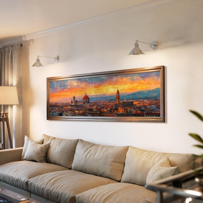Pu&ograve; includere: Dipinto di paesaggio incorniciato raffigurante un paesaggio urbano al tramonto. L'opera presenta una calda tavolozza di colori arancioni, rossi e blu, con dettagli architettonici. Il dipinto &egrave; montato sopra un divano beige in un soggiorno.