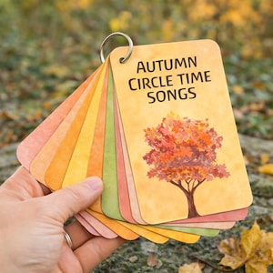 May include: A set of flashcards held together by a metal ring. The cards display the text "AUTUMN CIRCLE TIME SONGS" and a tree illustration. The cards feature a gradient of autumn colours, including orange, yellow, and green.