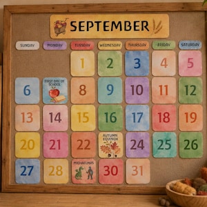 Op de afbeelding: Een prikbord met houten lijst toont een septemberkalender met kleurrijke, vierkante datumkaartjes in aquarel-stijl. De kalender bevat illustraties voor de eerste schooldag, de herfstequinox en Sint-Michaël, met de getallen één tot en met eenendertig.