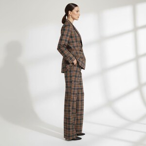 May include: A brown, black, and white plaid suit, including a blazer and wide-leg pants. The blazer has a notched lapel and a two-button closure. The pants are high-waisted. The suit is made of a woven fabric.