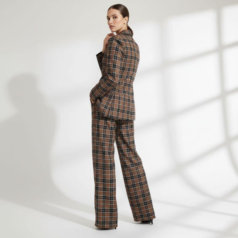 May include: A brown, black, and white plaid suit, including a blazer and wide-leg trousers. The blazer has a tailored fit, and the trousers are floor-length. The suit is made of a woven fabric, and the model is facing away from the camera.