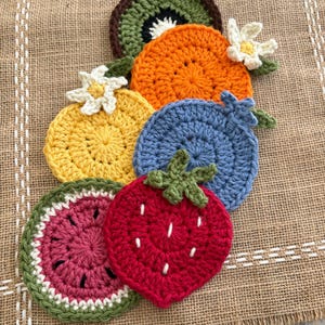 May include: A collection of colorful, crocheted fruit-shaped coasters. The set includes a watermelon, strawberry, kiwi, orange, lemon, and blueberry. Each coaster is made with vibrant yarn and detailed with leaves and seeds.
