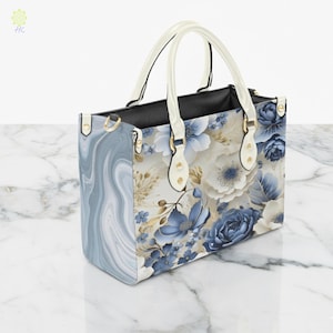 May include: A floral print handbag with a marble-like pattern on the side. The bag features white handles and gold-colored hardware. The floral design includes blue and white flowers with gold accents. The bag is rectangular and appears to be made of leather.