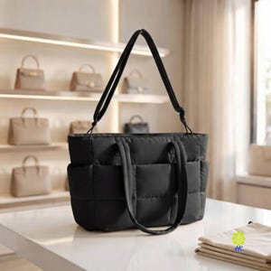 May include: A black quilted tote bag with a grid pattern, featuring two short top handles and a longer shoulder strap. The bag has a rectangular shape with visible exterior pockets on the front and sides, constructed from a soft, padded material.