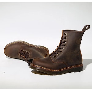 May include: Two brown leather boots with laces, eyelets, and pull tabs. The boots have a classic design with visible stitching and a sturdy sole. The boots are displayed on a white background.