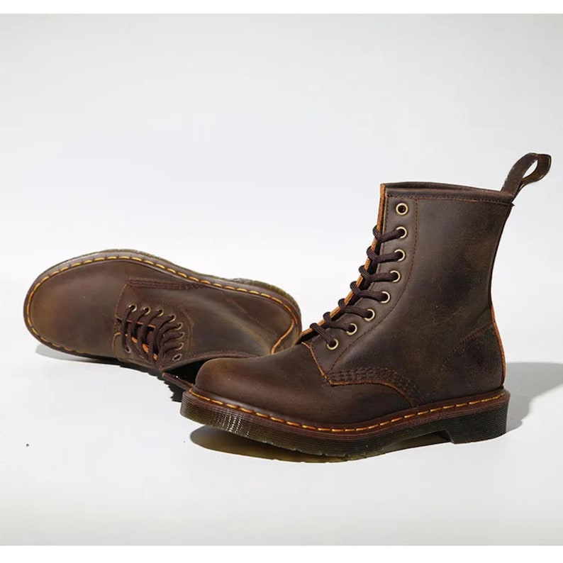 May include: Two brown leather boots with laces, eyelets, and pull tabs. The boots have a classic design with visible stitching and a sturdy sole. The boots are displayed on a white background.