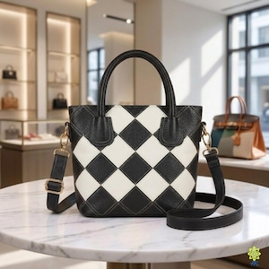 Könnte beinhalten: Eine strukturierte Handtasche mit einem schwarz-weißen Rautenmuster und einer genarbten Textur. Die Tasche verfügt über zwei Tragegriffe, einen abnehmbaren schwarzen Schulterriemen mit goldfarbenen Beschlägen und eine obere Öffnung.