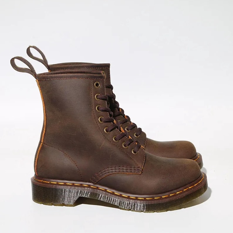 May include: A pair of brown leather boots with a lace-up design. The boots have a sturdy sole with yellow stitching and pull tabs at the top. The boots are made of a distressed leather material.