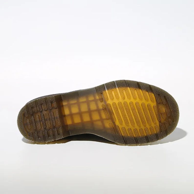 May include: A close-up of the sole of a black boot, showcasing the distinctive yellow and brown tread pattern. The sole is made of a durable material, with a grid-like design for grip. The boot's design is visible, with a focus on the sole's construction.