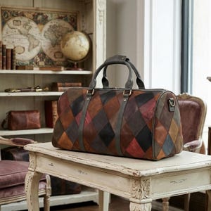 Könnte beinhalten: Eine große, mehrfarbige Leder-Duffel-Tasche mit einem Rauten-Patchwork-Design. Die Tasche hat einen oberen Griff und einen Schultergurt und steht auf einem weißen Tisch. Die Farben der Tasche sind Braun, Rot und Schwarz.
