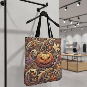 May include: A Halloween-themed tote bag with a detailed design. The bag features a carved orange pumpkin with a grinning face, surrounded by autumn leaves and swirling patterns in shades of brown, orange, and purple. Black handles.