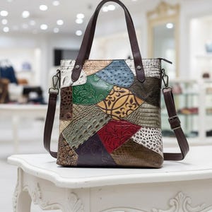 Könnte beinhalten: Eine mehrfarbige Patchwork-Ledertasche mit braunem Ledergriff und abnehmbarem Schultergurt. Die Tasche hat verschiedene Texturen und Farben, darunter Grün, Blau und Rot. Die Tasche steht auf einem weißen Tisch.
