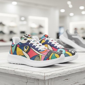 May include: A pair of colourful trainers with a vibrant abstract design. The shoes feature a mix of red, yellow, blue, and green patterns on a navy blue background, with white laces and soles. The trainers are displayed on a white wooden surface.
