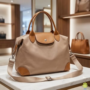 Puede incluir: Bolso de mano beige con detalles en cuero marr&oacute;n. El bolso tiene cierre de solapa, asas superiores y una correa para el hombro desmontable. Las esquinas y la solapa son de cuero marr&oacute;n. El bolso est&aacute; sobre una superficie de m&aacute;rmol blanco.
