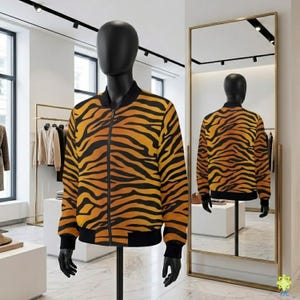 Può includere: Un giubbotto bomber a maniche lunghe caratterizzato da un vivace motivo a strisce tigrate arancioni e nere. Il capo presenta colletto, polsini e orlo a coste neri, con una chiusura frontale a zip integrale mostrata su un manichino.