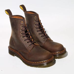 May include: A pair of brown leather boots with a lace-up design. The boots have a classic style with a rounded toe, a sturdy sole, and a pull tab at the back. The boots are approximately 8 inches tall.