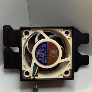 May include: A computer fan with a brown and beige fan blade, a black frame, and a blue and white label. The fan has a black wire and is set against a white background.