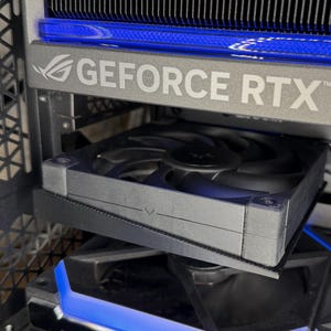 May include: A close-up of a computer component with the text "GEFORCE RTX" in silver. The component has a black fan and blue LED lighting. The computer case has a geometric design.