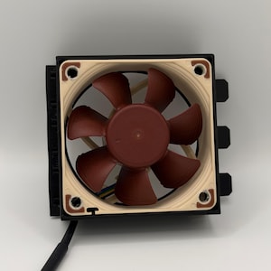 May include: A computer fan with a brown fan and blades, set in a beige and black frame. The fan has seven blades and is connected to a black cable. The fan is designed for cooling computer components.
